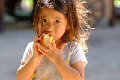 Portrait of girl eating apple while standing on road