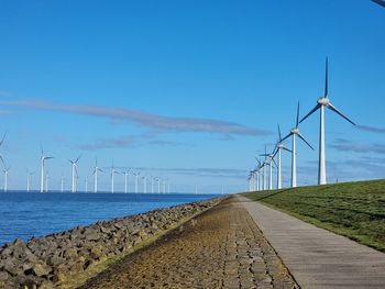 Wind turbines on landscape against blue sky