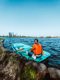 Man sitting on boat in sea against clear blue sky