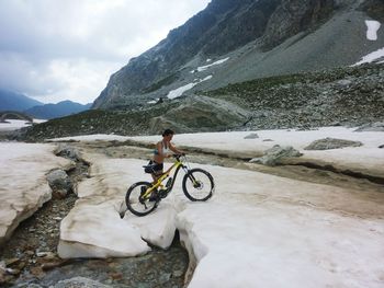 Full length of woman walking with mountain bike on snow against mountains