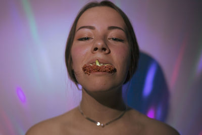 Close-up portrait of young woman eating fruit against wall