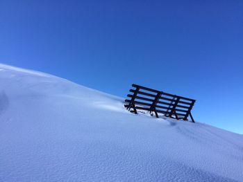 Low angle view of sled on snow covered hill against clear blue sky