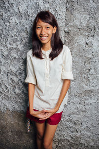 Portrait of young woman standing against wall