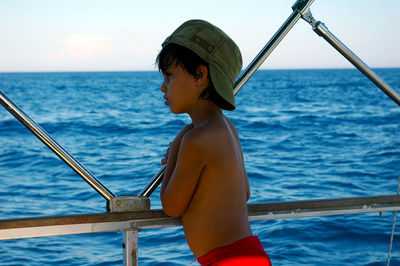 Side view of shirtless boy looking at sea by railing