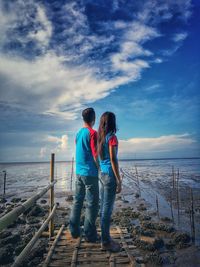 Rear view of couple standing at beach during sunset