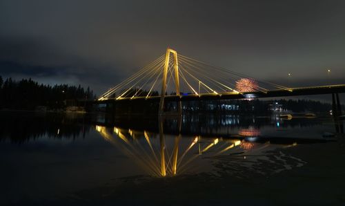 Illuminated bridge over river against sky at night