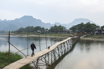 Tourists and a dog cross song river on a wooden bridge in the morning at vang vieng, laos