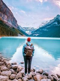 Man standing on rock by lake against sky