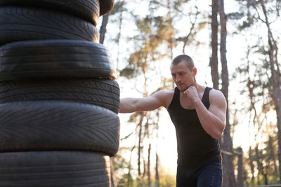 Young man exercising with tires in forest