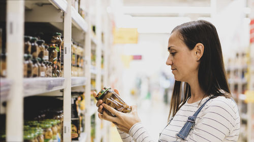 Side view of woman looking at bottle in supermarket