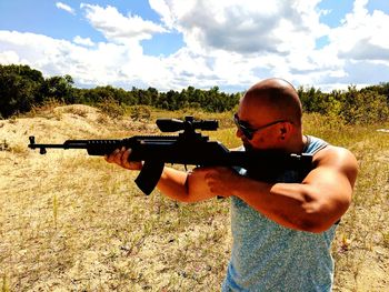 Man shooting with rifle on field against sky