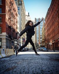 Full length of young woman jumping against buildings in city