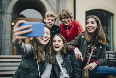 Smiling friends taking selfie through mobile phone in city