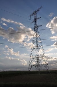 Electricity pylon on field against cloudy sky