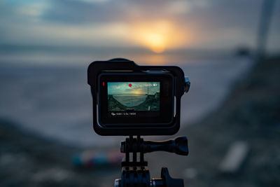 Close-up of digital camera against sky during sunset