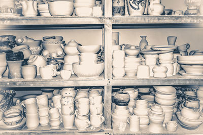 Bright pottery. many white, not painted clay pottery standing on wooden shelves