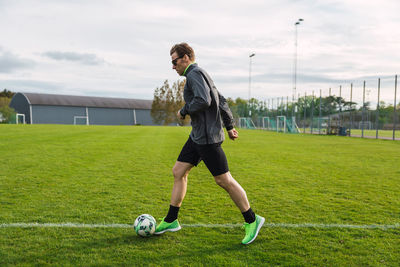 Side view of male soccer player in sportswear kicking ball during training in green football field