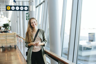 Young woman using phone while standing on laptop