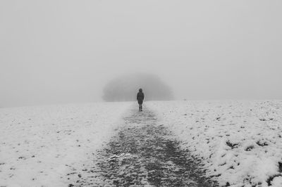 Rear view of woman walking on snowy field during foggy weather