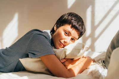 A woman lies on a bed in bright sunlight from the window.