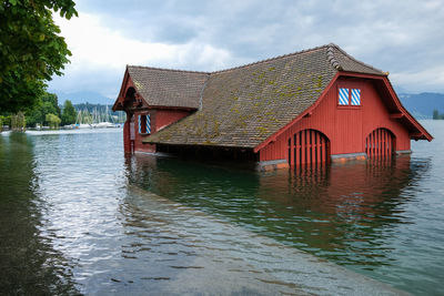 Stilt house on lake by building against sky