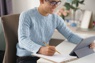 Midsection of man holding mobile phone while sitting on table