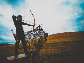 Man playing archery while standing on field against sky