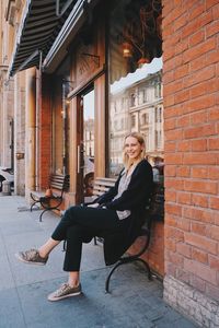 Portrait of smiling woman sitting on bench against brick wall