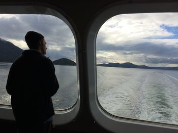 Rear view of man looking at sea seen through window