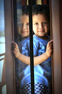 Portrait of cute boy hiding near glass window