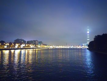 Illuminated city by sea against sky at night