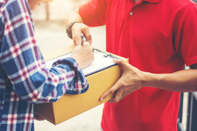 Midsection of female customer signing receipt while receiving package from delivery man outdoors