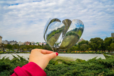 Midsection of person holding plant against sky