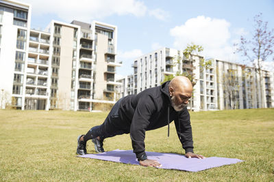 Bald man doing push ups on exercise mat at park