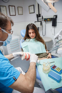 Professional doctor demonstration process of healthy teeth brushing to young woman sitting in chair.