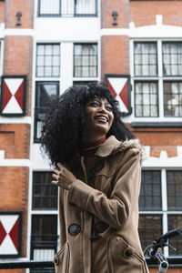 Happy woman with curly hair standing in front of building