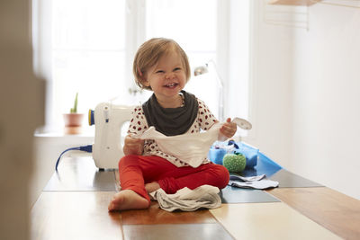 Cheerful girl wearing scarf while sitting on table against sewing machine at home