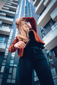 Low angle view of young woman standing against buildings in city