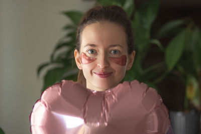 Woman with pink patches in heart shape under eyes holds pink balloon. birthday or valentines day.