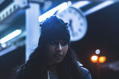 Close-up of thoughtful young woman standing at railroad station during night