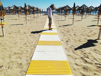 Mature man looking down while standing at beach during sunny day