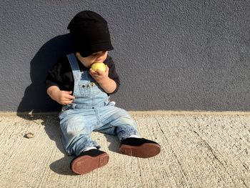 High angle view of baby boy eating fruit while sitting against wall