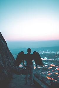 Rear view of man wearing costume wing standing at mountain against sky at dusk