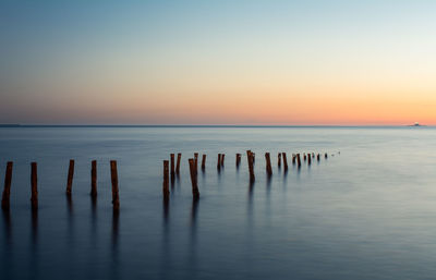 Wooden posts in sea against sky during sunset