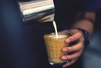 Cropped image of hand pouring milk in coffee
