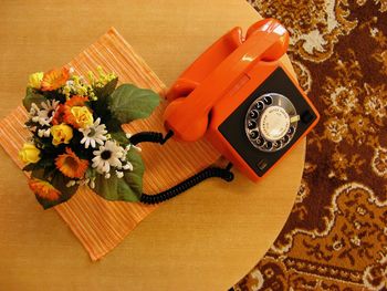 Directly above shot of orange old-fashioned telephone by flowers on table