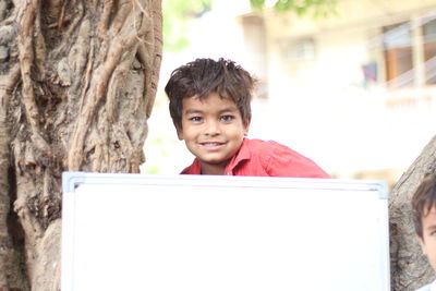 Portrait of boy smiling on tree trunk