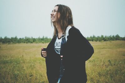 Happy woman holding jacket while standing on field against sky