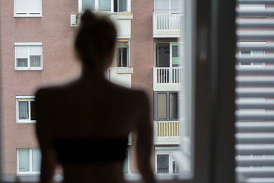 Rear view of woman looking through window at home