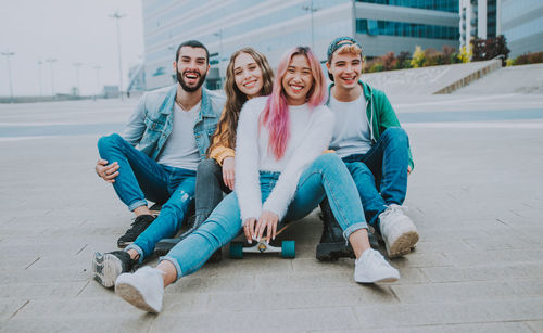 Portrait of cheerful friends sitting against building outdoors